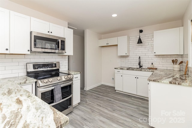 kitchen with backsplash, white cabinets, hanging light fixtures, sink, and appliances with stainless steel finishes