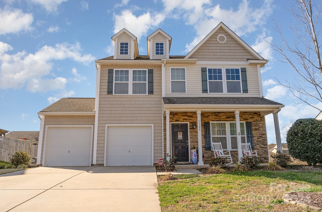 view of front of house featuring covered porch, a front yard, and a garage