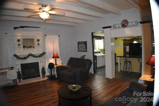 living room featuring beam ceiling, ceiling fan, and dark wood-type flooring