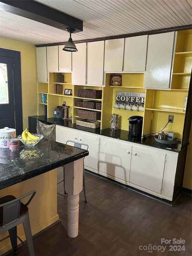 kitchen featuring white cabinets, a breakfast bar, decorative light fixtures, and dark wood-type flooring