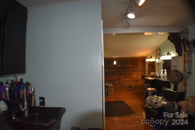 bathroom featuring sink, rail lighting, wood walls, wood-type flooring, and lofted ceiling