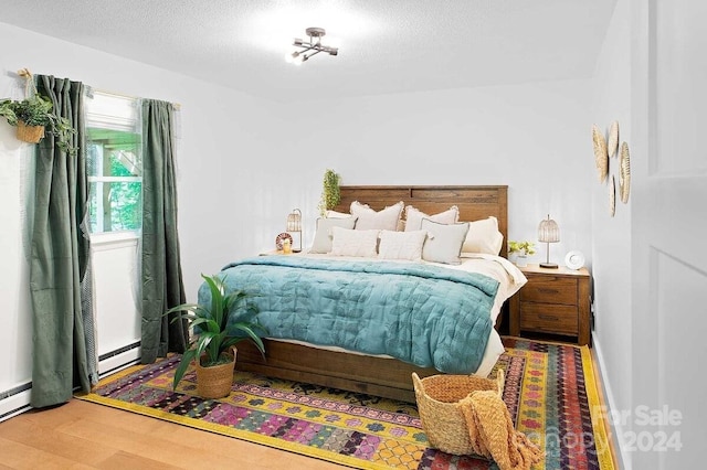 bedroom with a textured ceiling, hardwood / wood-style flooring, and a baseboard radiator