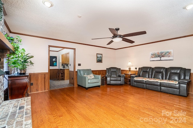 living room featuring crown molding, wooden walls, ceiling fan, a textured ceiling, and wood-type flooring