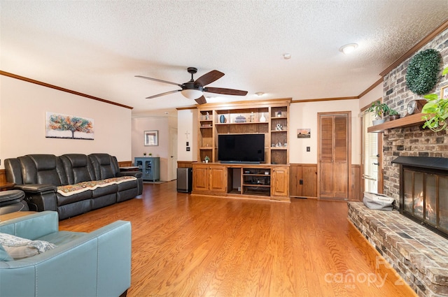 living room featuring ceiling fan, wood-type flooring, a textured ceiling, a fireplace, and ornamental molding