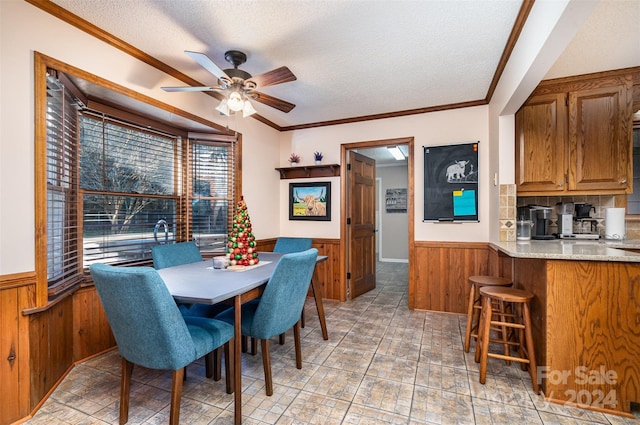 dining area featuring ornamental molding, a textured ceiling, ceiling fan, and wooden walls