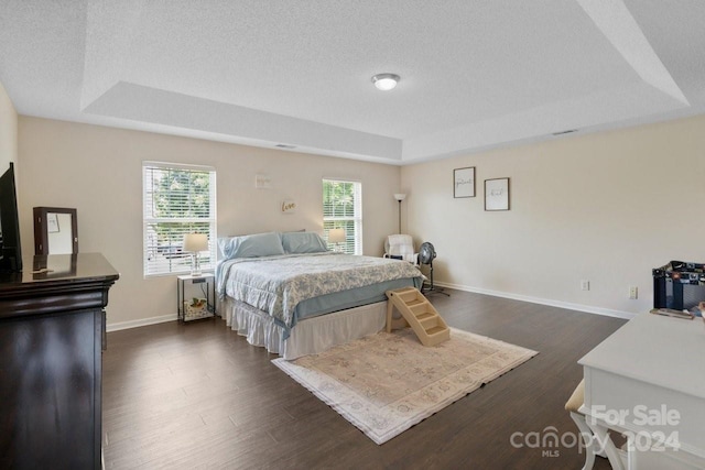 bedroom with a textured ceiling, a tray ceiling, and dark wood-type flooring