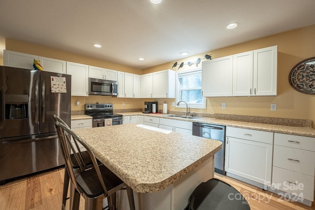 kitchen with light wood-type flooring, a kitchen island, a kitchen bar, white cabinetry, and stainless steel appliances