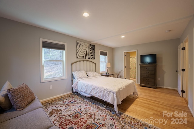 bedroom featuring ensuite bath, multiple windows, and light wood-type flooring