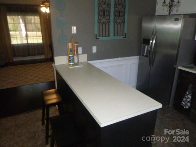 kitchen with a kitchen bar, stainless steel fridge with ice dispenser, white cabinets, and ceiling fan