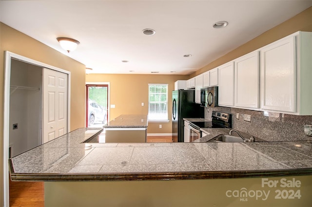 kitchen featuring hardwood / wood-style floors, backsplash, black appliances, kitchen peninsula, and white cabinetry