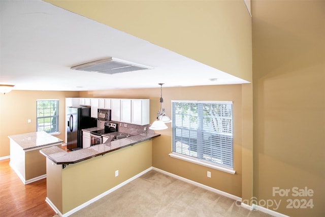 kitchen with kitchen peninsula, a breakfast bar, black appliances, pendant lighting, and white cabinets