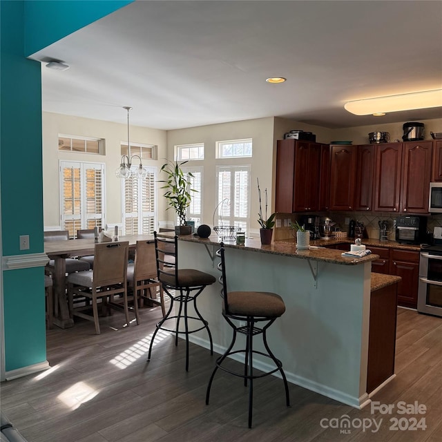 kitchen with backsplash, dark wood-type flooring, an inviting chandelier, hanging light fixtures, and stainless steel appliances