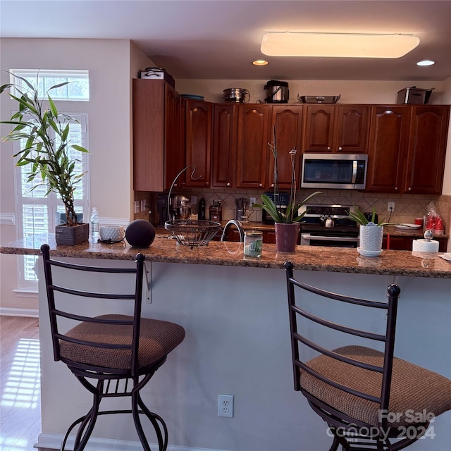 kitchen featuring dark stone counters, a kitchen breakfast bar, sink, decorative backsplash, and appliances with stainless steel finishes