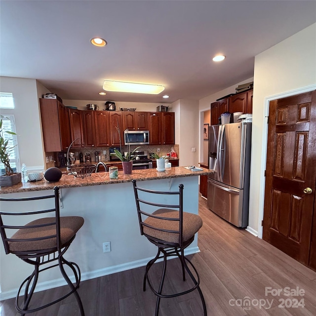 kitchen featuring dark stone counters, decorative backsplash, light wood-type flooring, appliances with stainless steel finishes, and kitchen peninsula