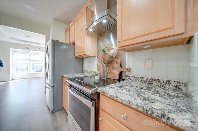 kitchen featuring light stone counters, stainless steel range with electric stovetop, wall chimney exhaust hood, light brown cabinets, and an inviting chandelier