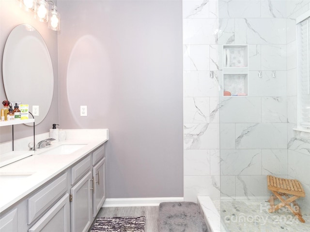 bathroom with a tile shower, vanity, and wood-type flooring