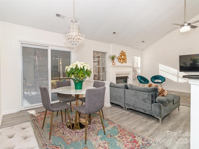 dining area featuring ceiling fan with notable chandelier, light wood-type flooring, lofted ceiling, and a high end fireplace