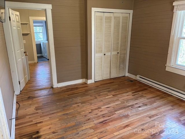 unfurnished bedroom featuring hardwood / wood-style floors, a closet, wooden walls, and multiple windows