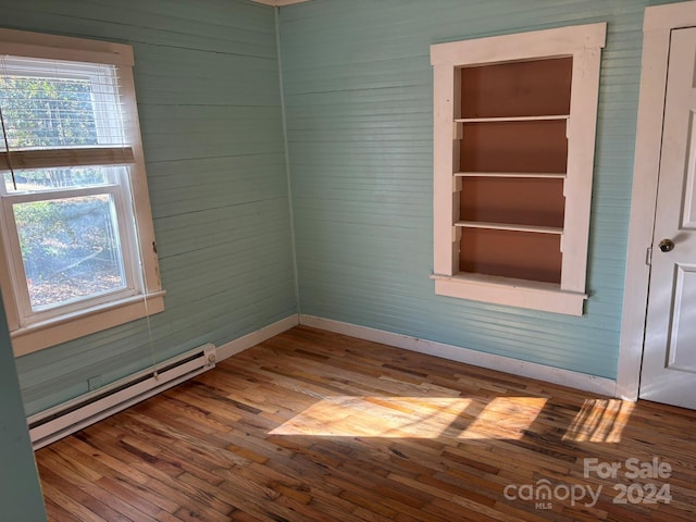 unfurnished room with baseboard heating, plenty of natural light, and wood-type flooring