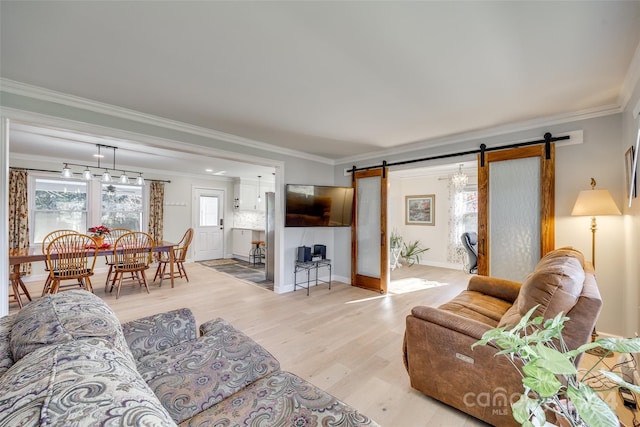 living room with a barn door, light wood-type flooring, and ornamental molding