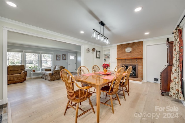 dining space featuring a brick fireplace, ornamental molding, and light wood-type flooring