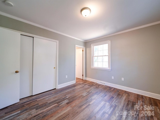 unfurnished bedroom featuring dark hardwood / wood-style floors, ornamental molding, and a closet