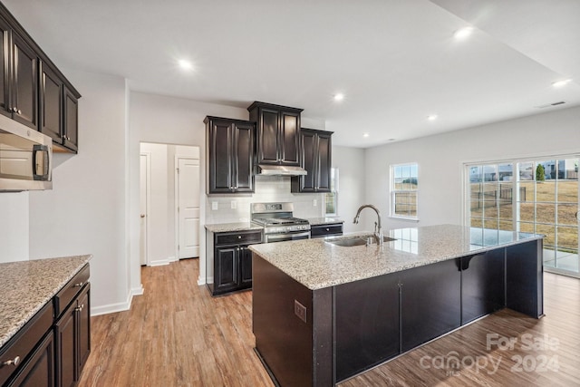 kitchen featuring a center island with sink, sink, light hardwood / wood-style flooring, light stone counters, and stainless steel appliances