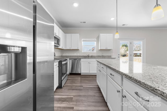 kitchen with appliances with stainless steel finishes, pendant lighting, white cabinetry, light stone counters, and crown molding