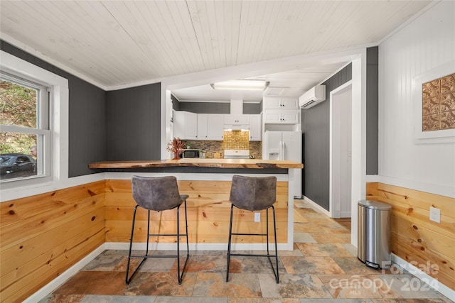 kitchen featuring wood walls, white appliances, tasteful backsplash, a kitchen bar, and white cabinetry