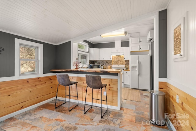 kitchen with white cabinets, plenty of natural light, wood walls, and white appliances