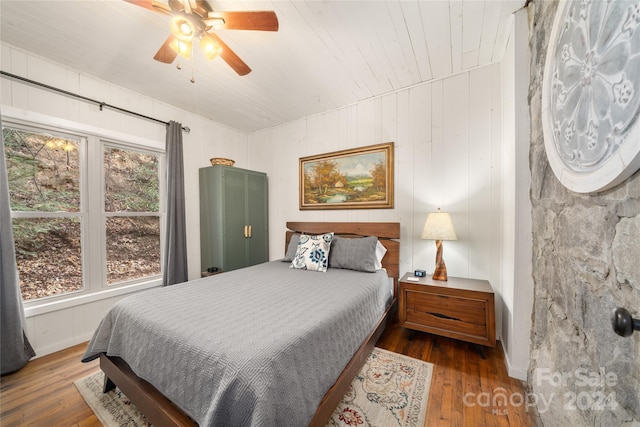 bedroom with hardwood / wood-style flooring, ceiling fan, and wood walls