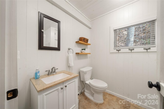 bathroom with tile patterned flooring, wood walls, toilet, vanity, and ornamental molding