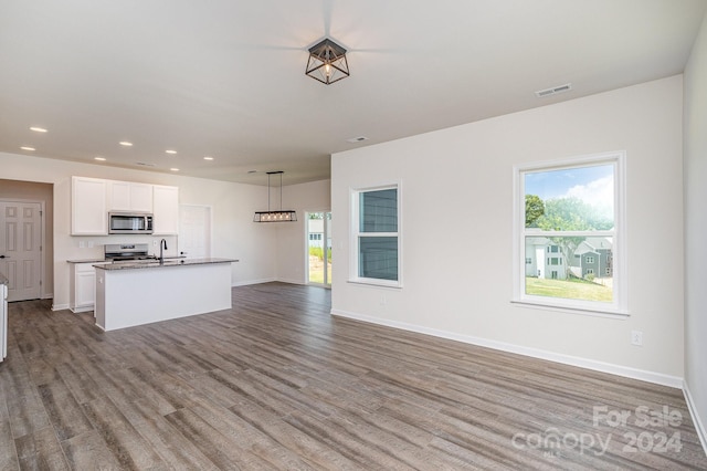 kitchen featuring appliances with stainless steel finishes, a kitchen island with sink, white cabinets, hardwood / wood-style floors, and hanging light fixtures