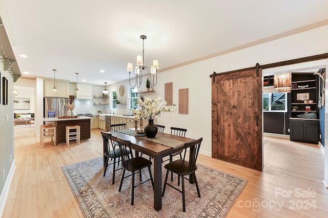 dining space with sink, crown molding, a barn door, light hardwood / wood-style floors, and a chandelier