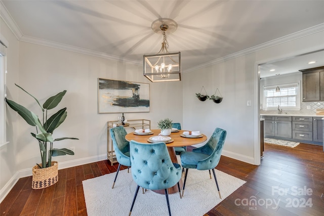 dining space featuring sink, crown molding, dark wood-type flooring, and an inviting chandelier