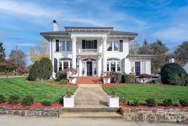 greek revival inspired property featuring a balcony and a front lawn