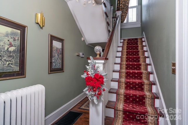 stairs with radiator, crown molding, wood-type flooring, and vaulted ceiling