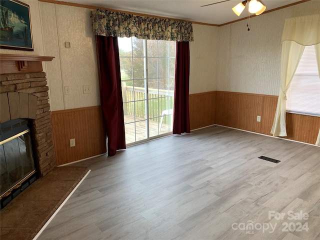 unfurnished living room with wood-type flooring, wooden walls, ceiling fan, and crown molding