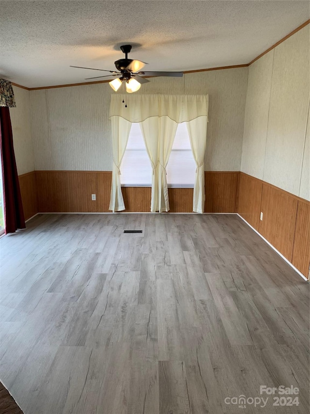 spare room featuring hardwood / wood-style floors, wood walls, crown molding, ceiling fan, and a textured ceiling