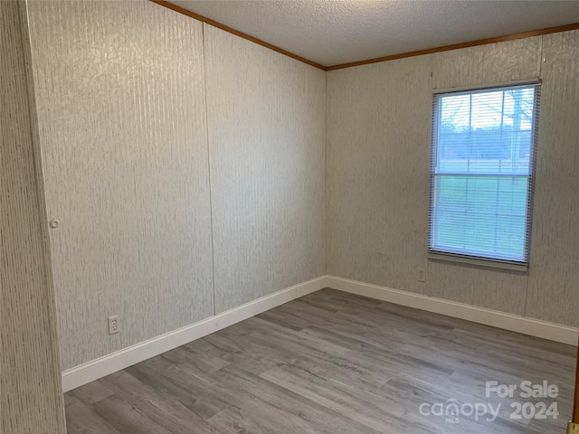 spare room featuring wood-type flooring, a textured ceiling, and crown molding