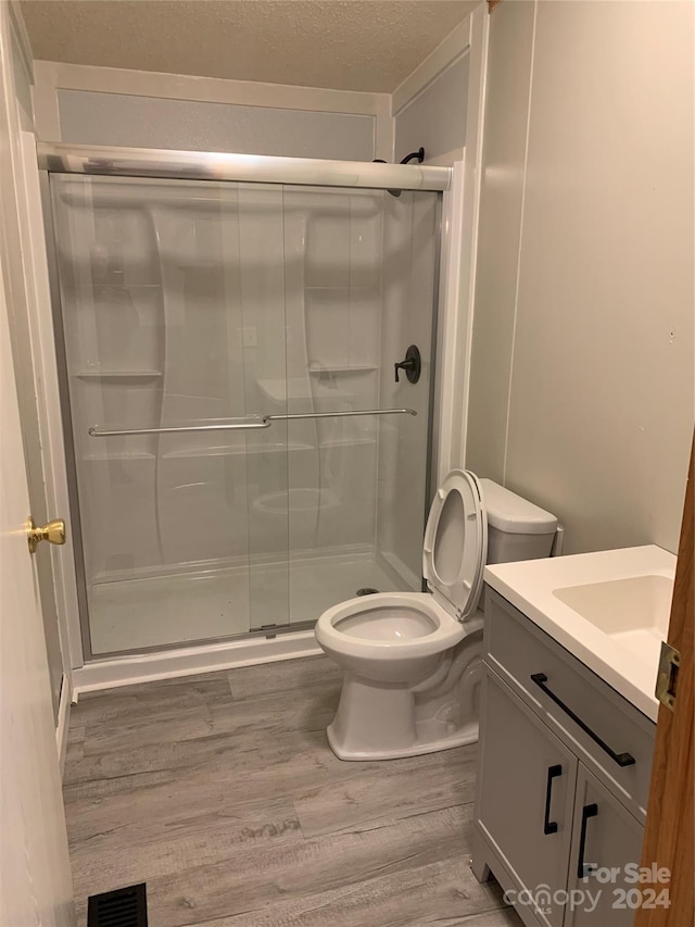 bathroom with hardwood / wood-style floors, vanity, toilet, walk in shower, and a textured ceiling