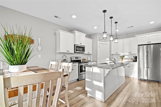 kitchen with light stone counters, stainless steel appliances, a center island with sink, light hardwood / wood-style flooring, and white cabinets