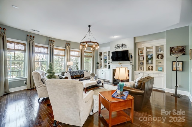 living room featuring dark wood-type flooring, an inviting chandelier, and built in shelves