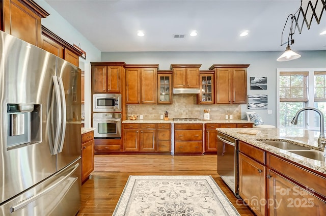 kitchen featuring sink, pendant lighting, stainless steel appliances, light stone countertops, and light hardwood / wood-style floors