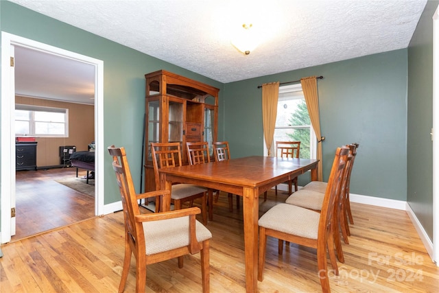 dining space with a healthy amount of sunlight, light wood-type flooring, and a textured ceiling