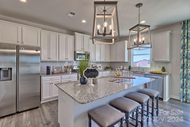 kitchen with a center island, white cabinets, hardwood / wood-style flooring, decorative light fixtures, and stainless steel appliances