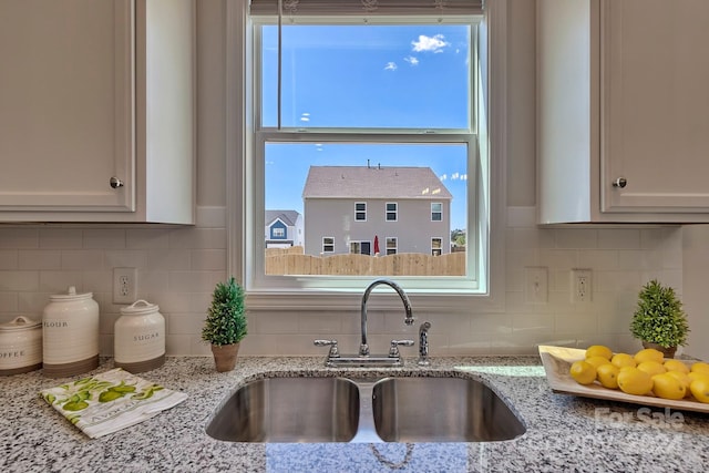 kitchen featuring decorative backsplash, light stone counters, and sink