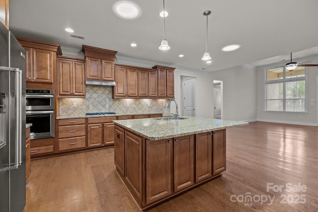 kitchen with sink, light stone countertops, an island with sink, appliances with stainless steel finishes, and decorative light fixtures