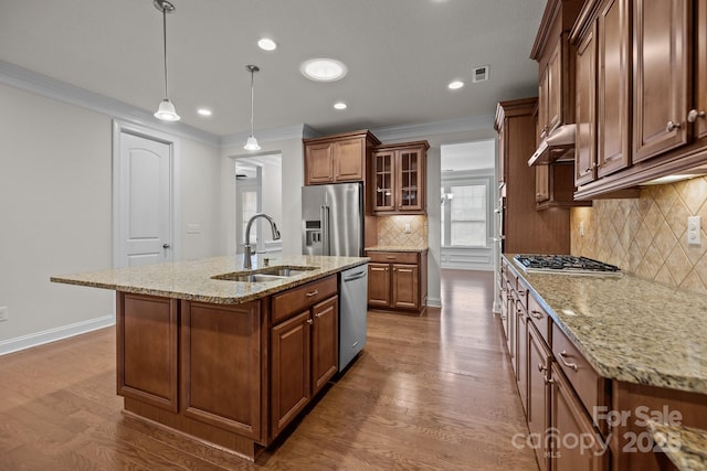 kitchen with sink, stainless steel appliances, pendant lighting, a center island with sink, and ornamental molding