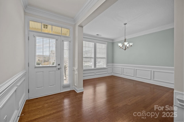 foyer entrance with ornamental molding, dark wood-type flooring, and a chandelier